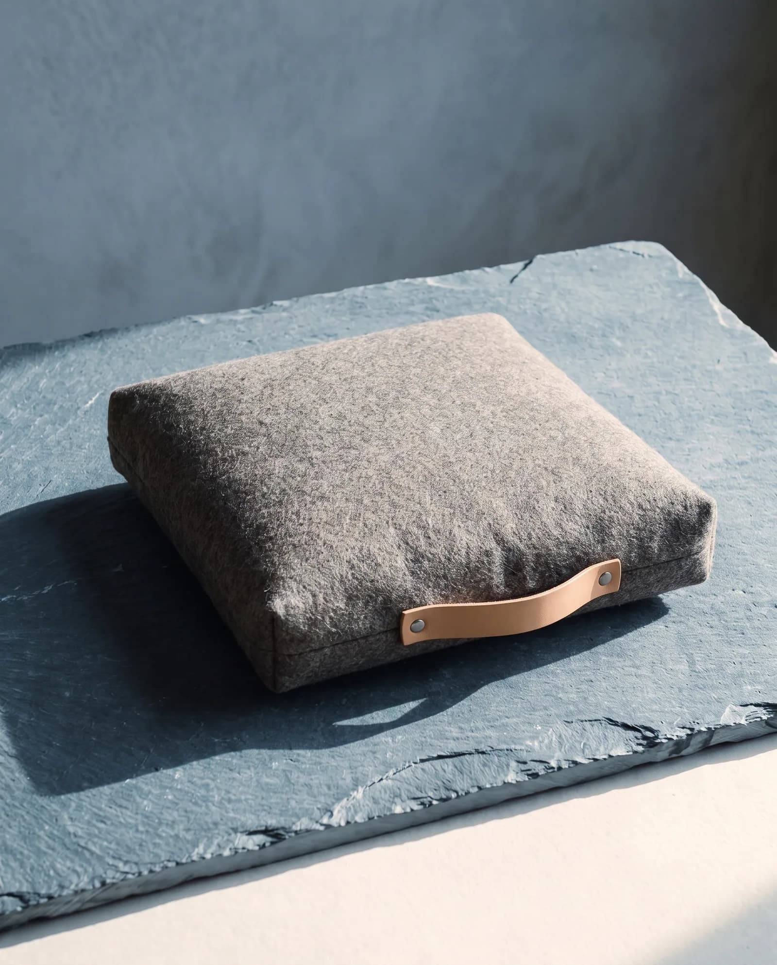 Wool Floor Cushion — Felt shell, wool fill, leather carry strap.